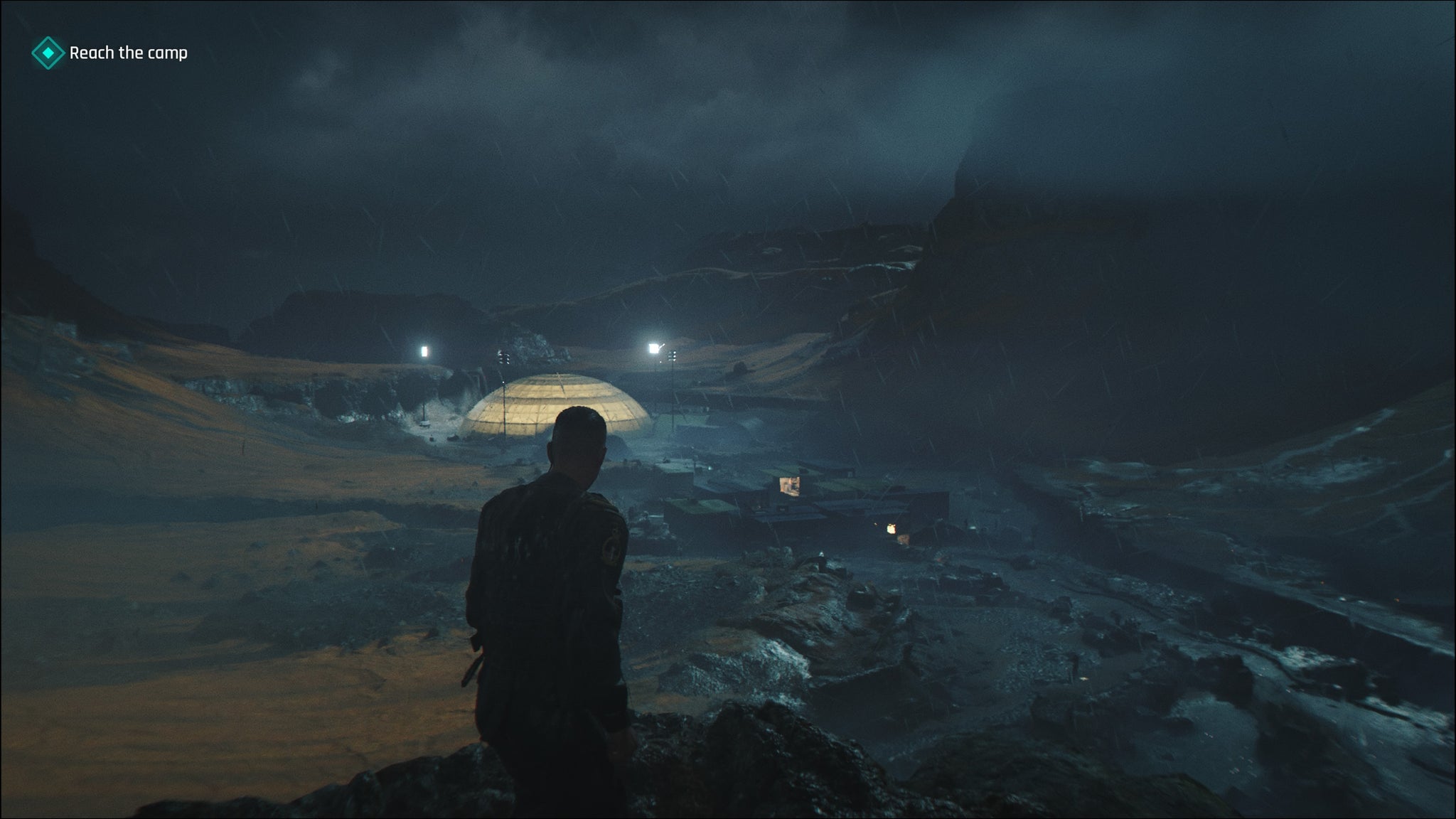 A screenshot of 007 First Light, showing Bond in Iceland overlooking an enemy encampment at night. A large, illuminated dome structure sits at the end of the camp.