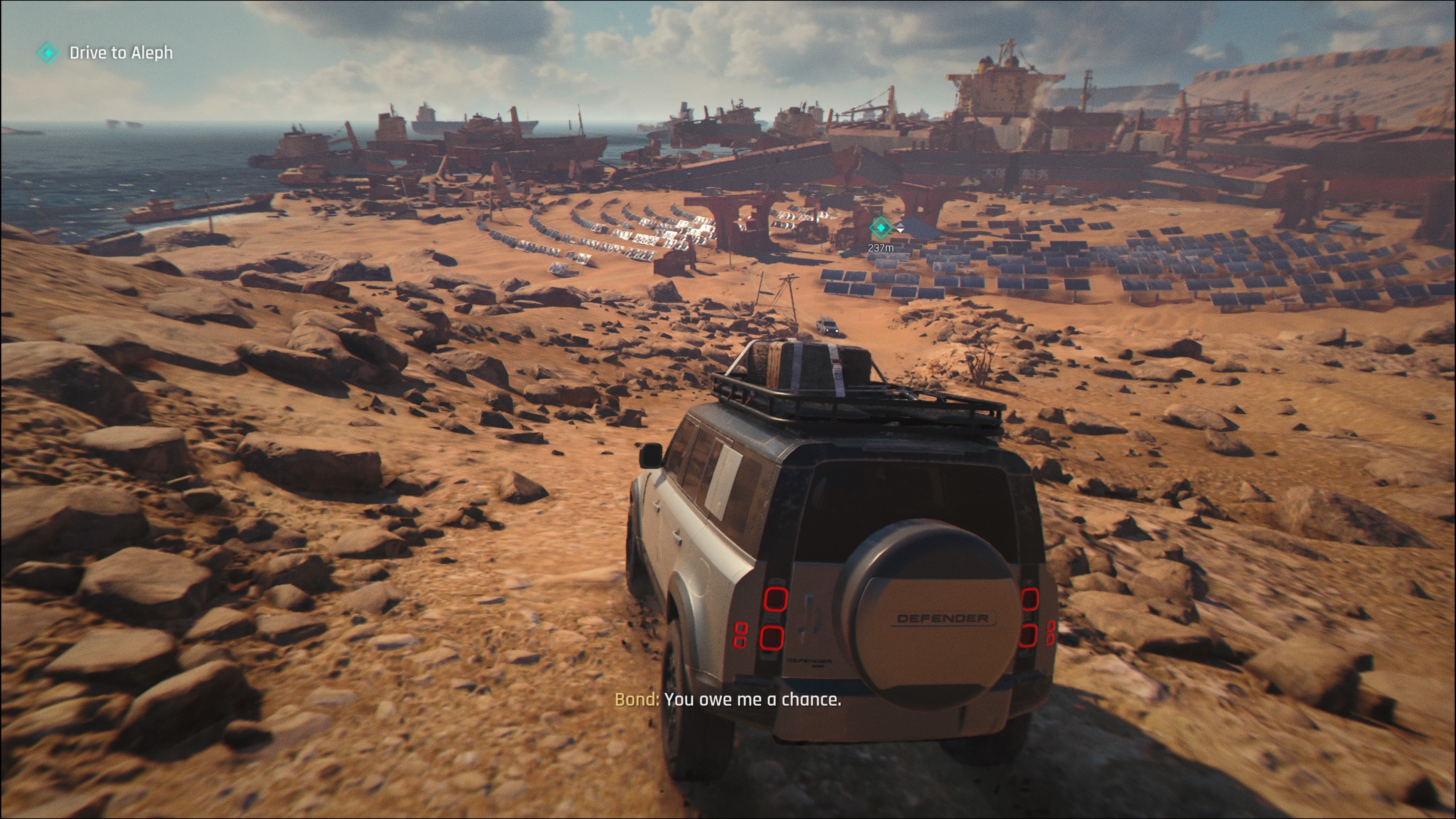 A screenshot of 007 First Light, showing a 4x4 driving through the ochre desert of Mauritania, headed toward a shipbreaking yard.