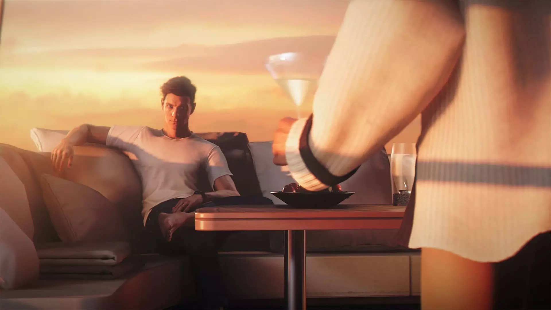 A young James Bond reclines on a sofa as a person in a white suit brings him a champagne glass.