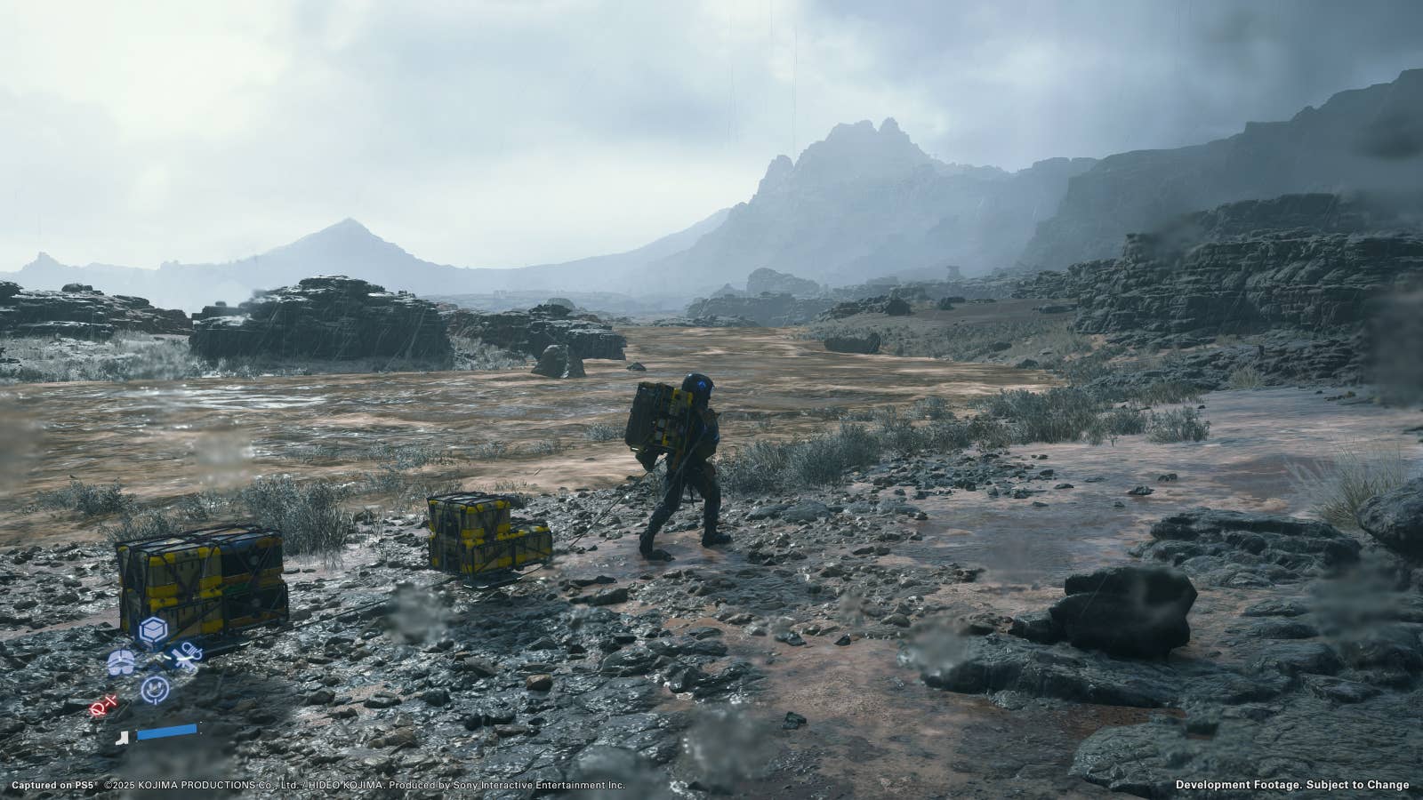 Death Stranding 2 screenshot showing Sam pulling multiple packages through a barren, desolate, grey rocky area