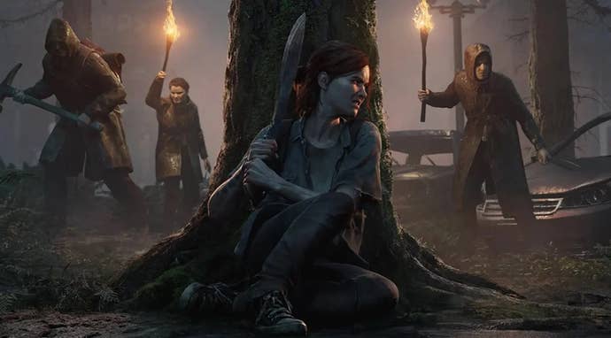 A woman hiding behind a tree with a machete while men with torches search for her in The Last Of Us Part 2