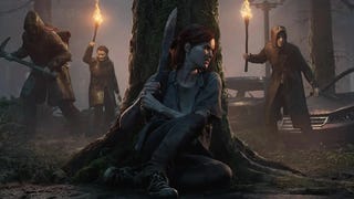 A woman hiding behind a tree with a machete while men with torches search for her in The Last Of Us Part 2