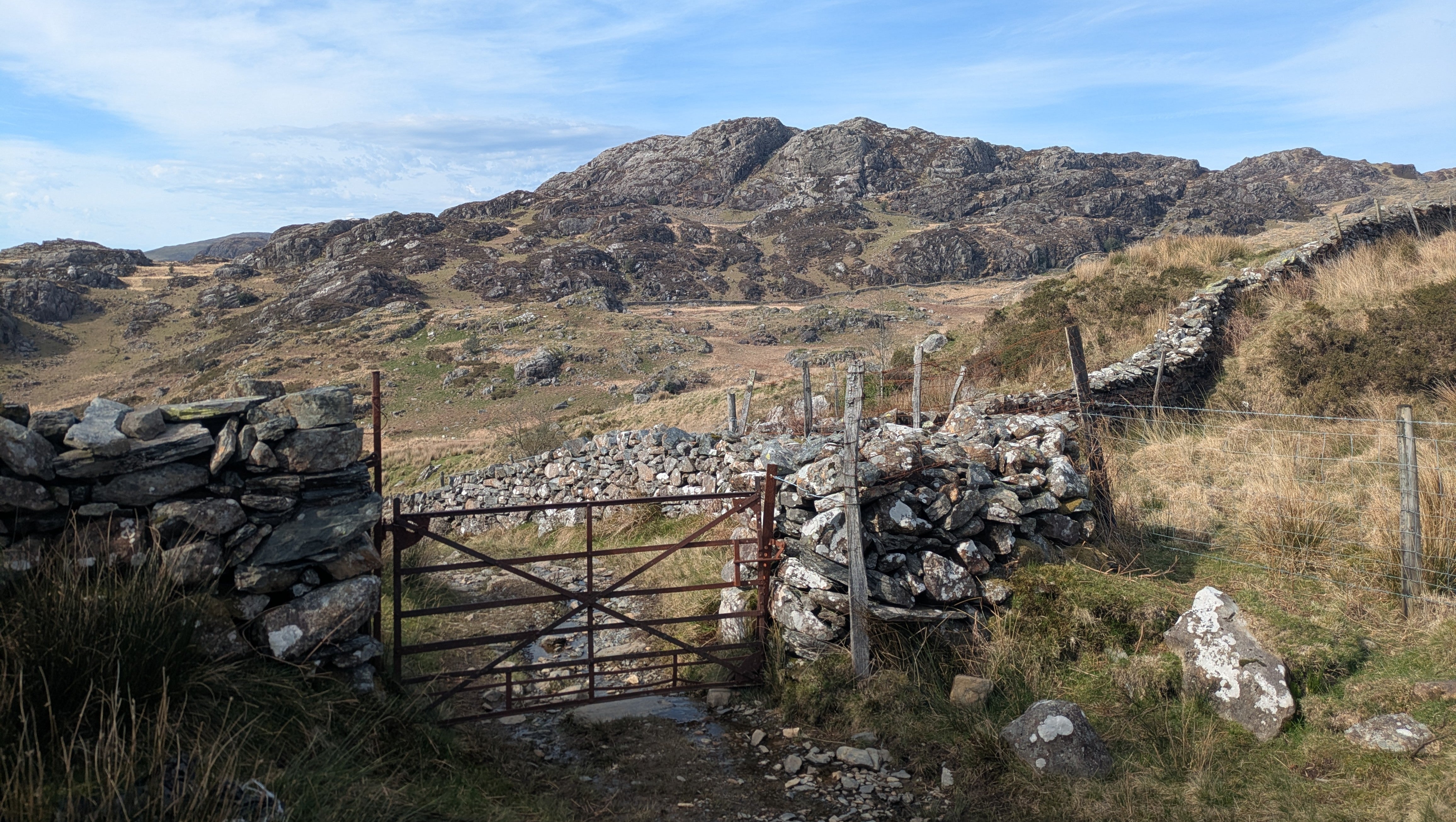 A view of a rocky mountain from a path with a gate in the foreground.