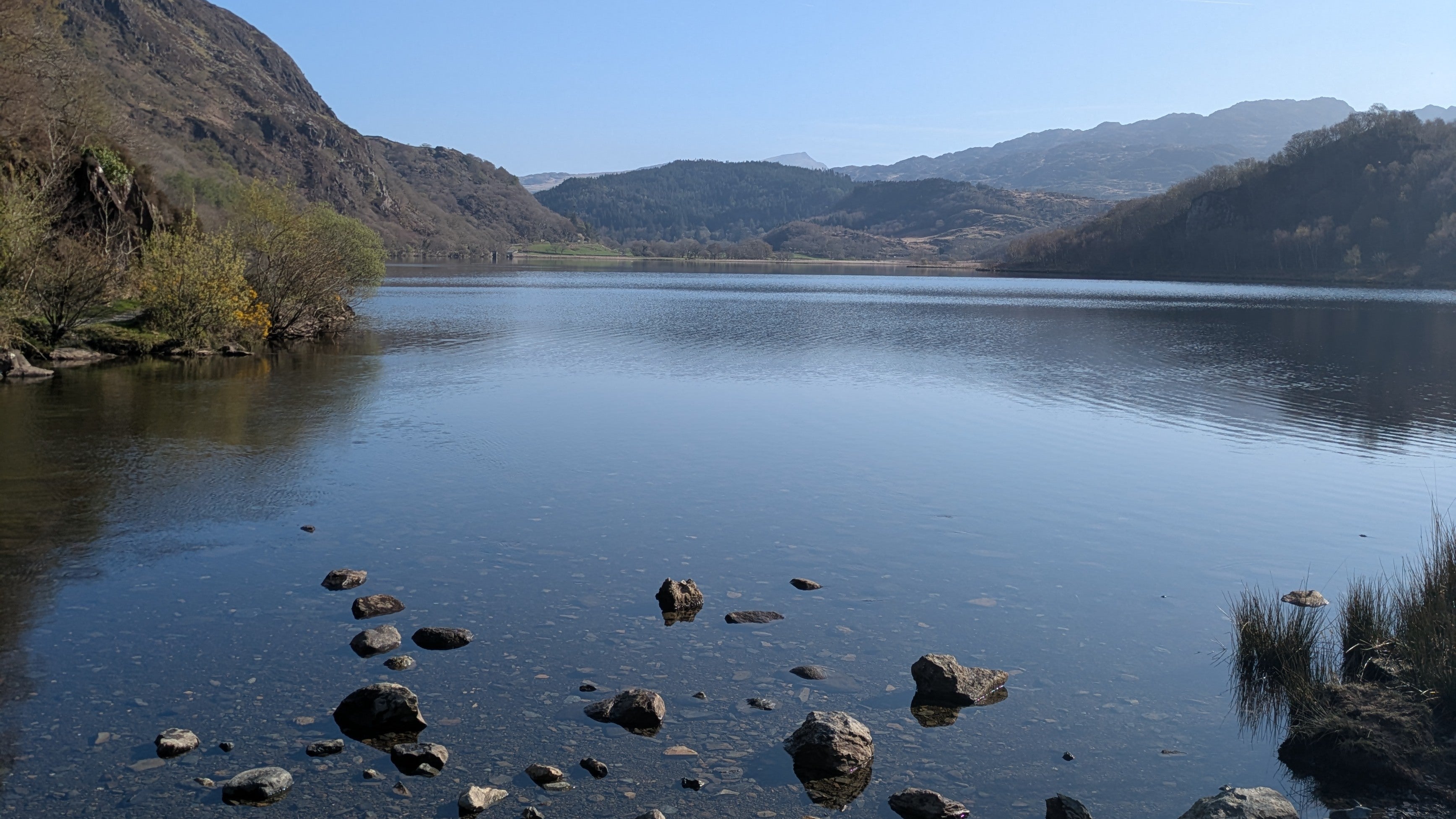 A lake surrounded by hills and mountains on a sunny day in Wales.