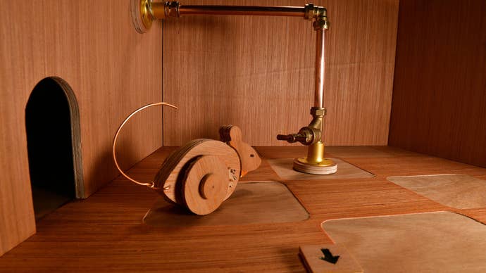 A wooden mouse on wheels investigating a valve on a brass pipe in a wooden chamber.
