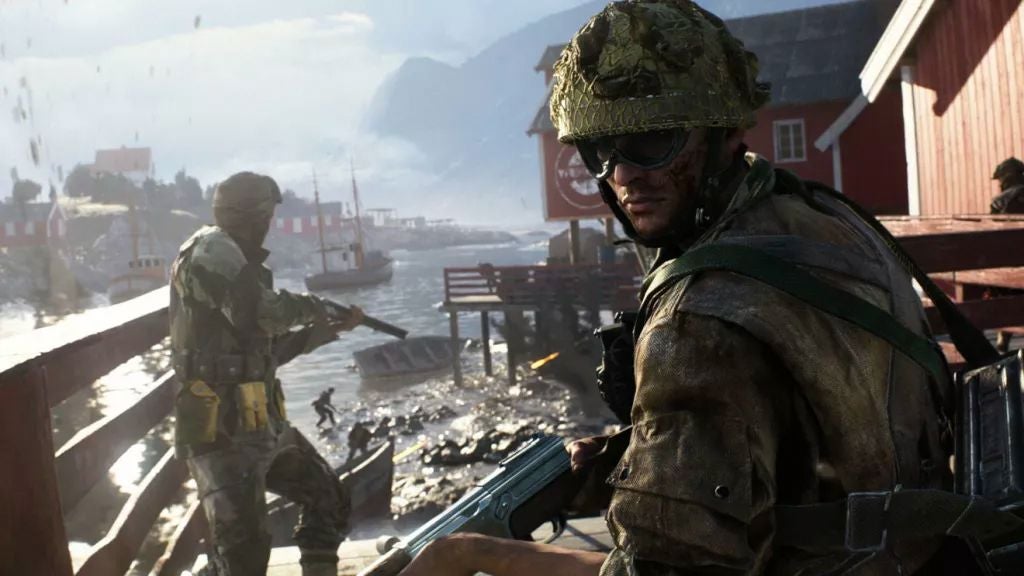 A soldier looking back at you while another looks at the land ahead on a riverside in Battlefield 6, with a house visible on the right - 1