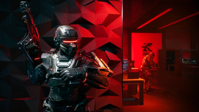 A warrior in a red-visored exosuit standing against a red-tinted wall with another soldier visible around the corner, from La Quimera
