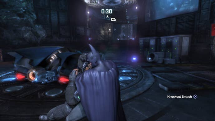 Batman chokes a goon by the Batmobile in the Batcave in this screen from Batman Arkham City