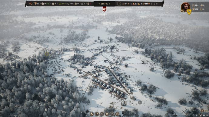 A Manor Lords screenshot. A zoomed out perspective on Bertie’s quite expansive village, in winter time. The surrounding pastoral lands and forests are carpeted in snow.