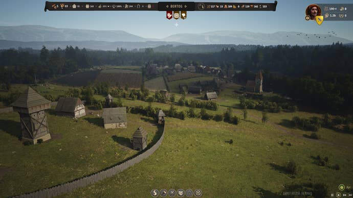 A zoomed-in screenshot of Bertie’s village in Manor Lords, as seen from the fenced perimeter of his protected manor. From this angle, we see the gently rolling hills and some of the height of the rows of small houses Bertie has built on top of it. He’s a skilled village planner, Bertie - he doesn’t get enough credit for it.