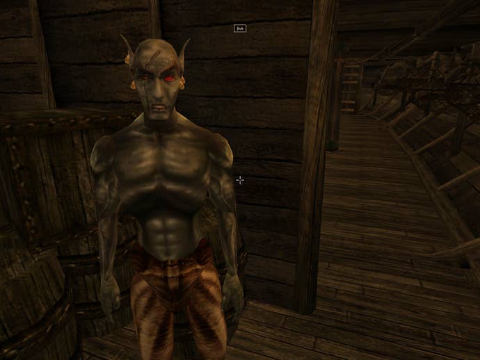 A screenshot from The Elder Scrolls 3: Morrowind showing a grey-skinned and red eyed and scarred sailor, who's shirtless and muscled, looking directly at the player. They are presumably a drow.