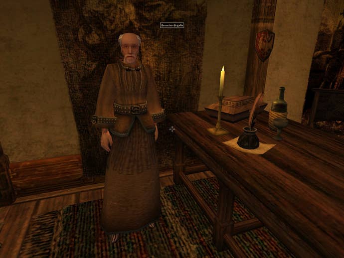 A screenshot from The Elder Scrolls 3: Morrowind showing an old man with light skin and grey hair and beard, and a brown robe, inside a neatly appointed office chamber of some kind.