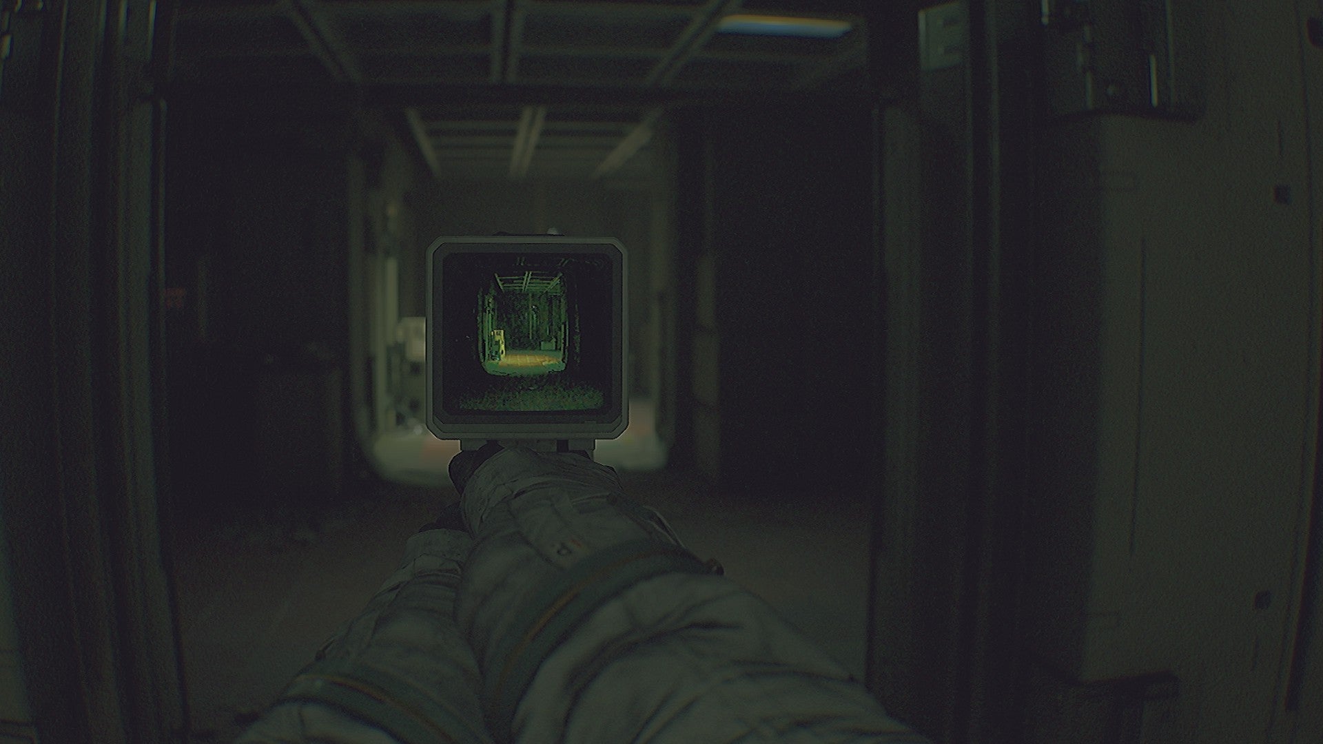 A first-person view of a dingy corridor with a device held out so that you can see the corridor through its tiny TV display, from horror game Routine. - 8