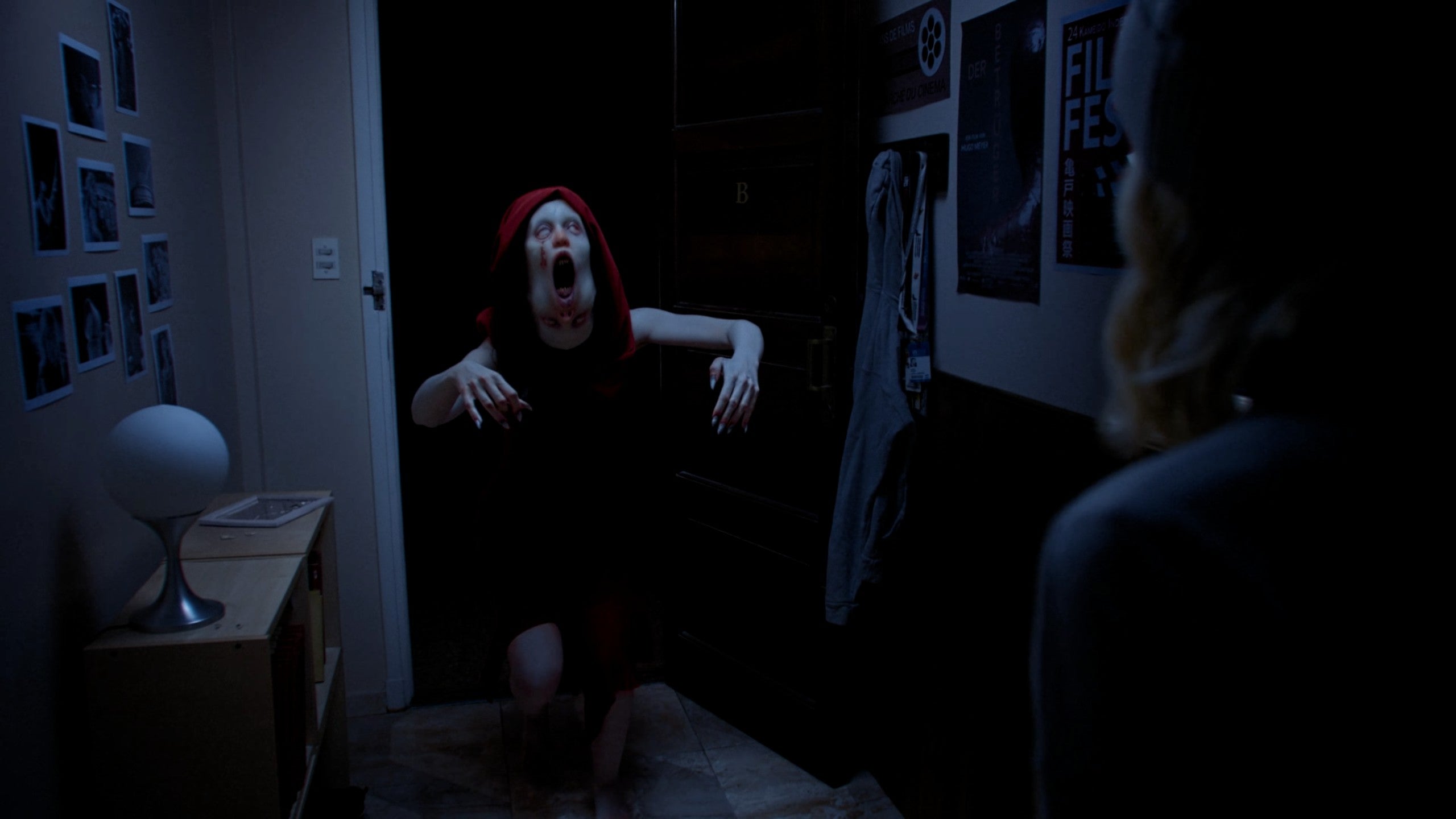 A live-action image of a strange, two-faced humanoid rushing in from a darkened door towards the camera.