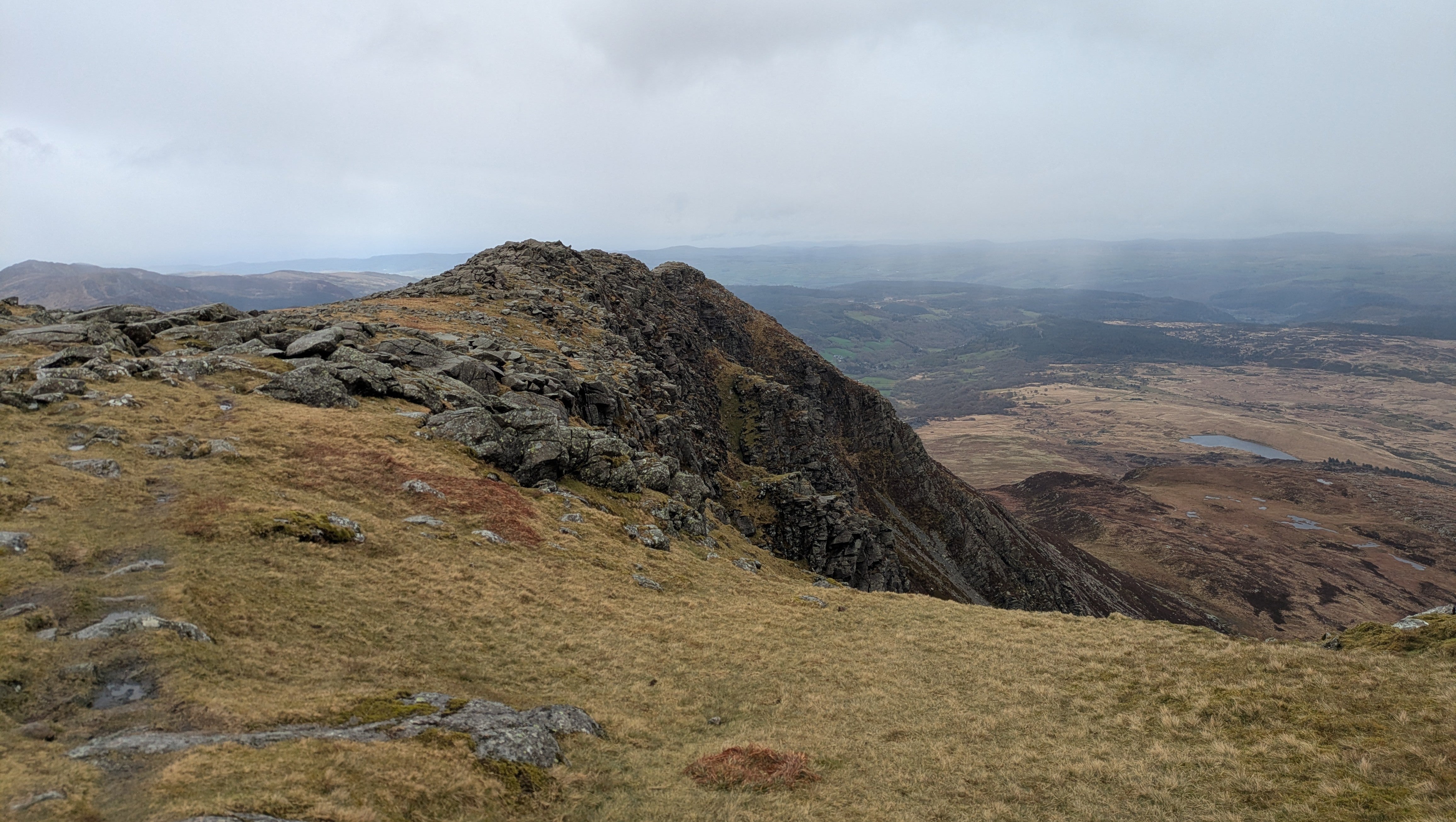 A green slope leading to a crag above wild countryside in Wales.
