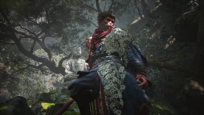 The Destined One, wearing a robe of armour composed of coins linked together, stands in front of a Buddha statue in this screenshot from Black Myth: Wukong.