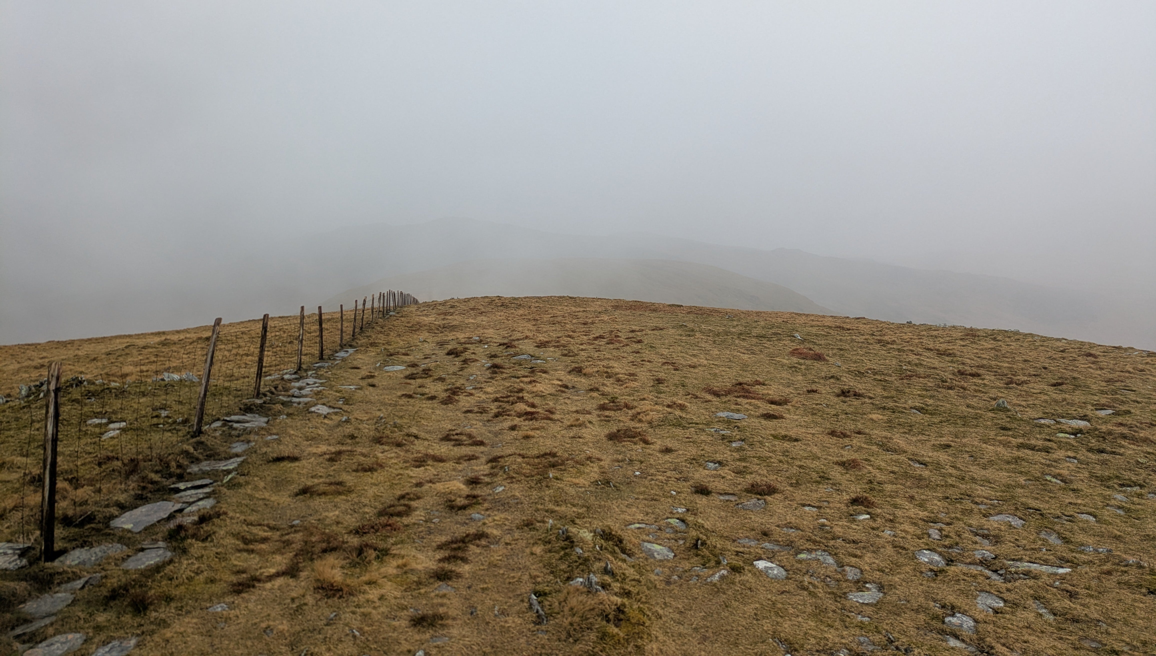 A misty grass ridge in the mountains of Wales with a fence running off into the distance.