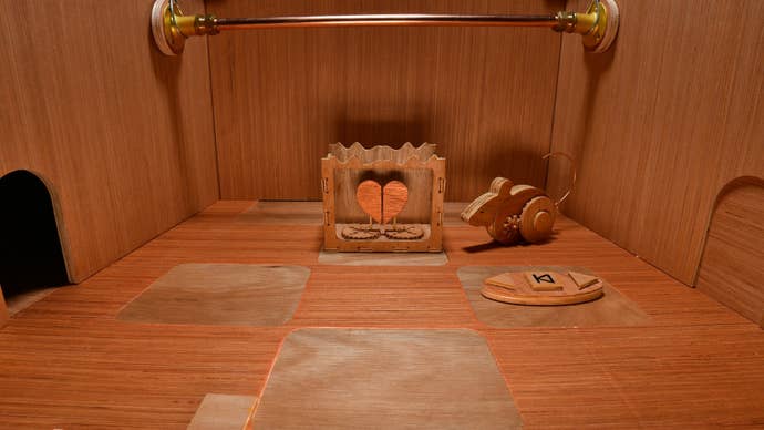 A wooden mouse on wheels next to a curious mechanical heart machine and some arrow floor panels in a wooden chamber.
