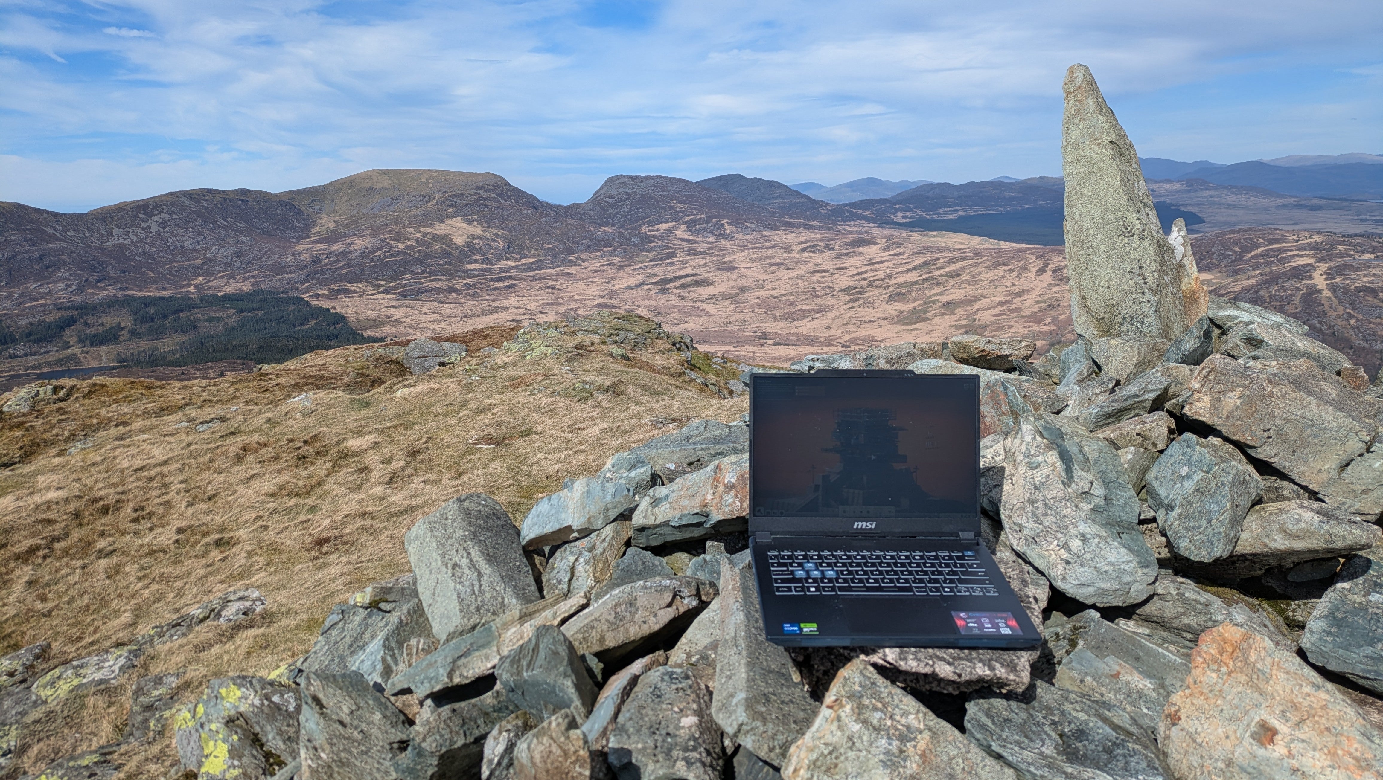 A laptop perched on a stone cairn on top of the mountain Y Garm, with other mountains in the distance.