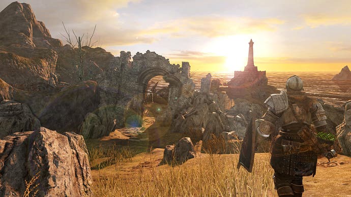 A sunset scene within Dark Souls 2, as the player character in a suit of armor looks out to the horizon behind a scene of towering rocks.