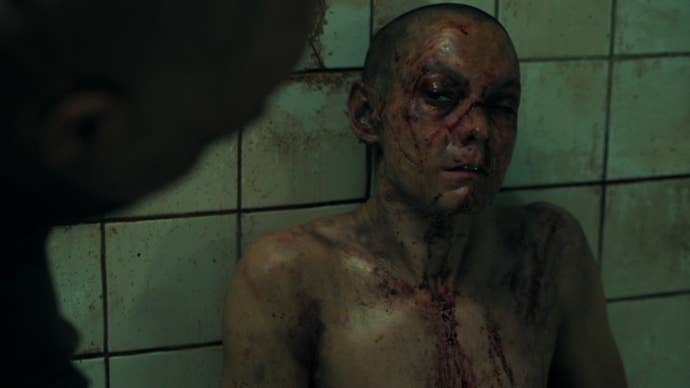 A naked Seraphite member sits beaten and bloody against a tiled wall in The Last of Us season two