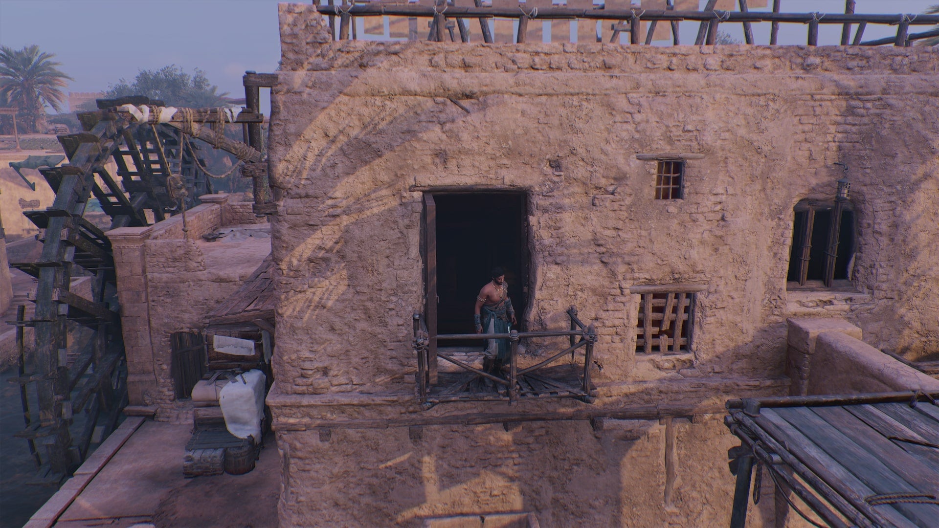 Basim stands on a small balcony outside of a watermill in Assassin's Creed Mirage - 1