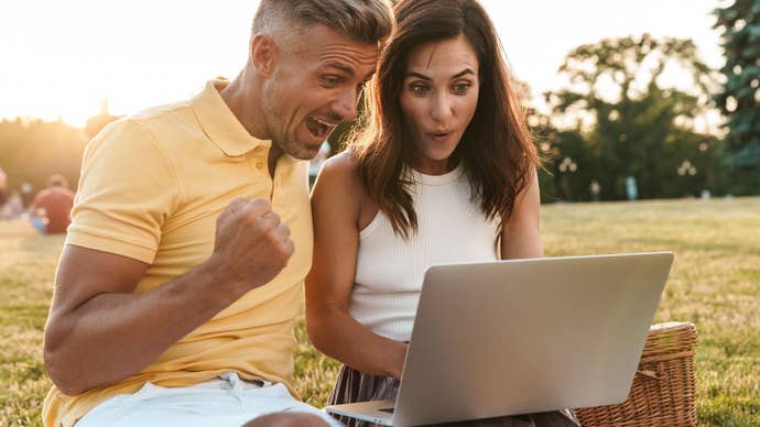 A ridiculous photograph of two middle-aged people sitting in a park and getting very excited about whatever it is they’re looking at on a laptop.