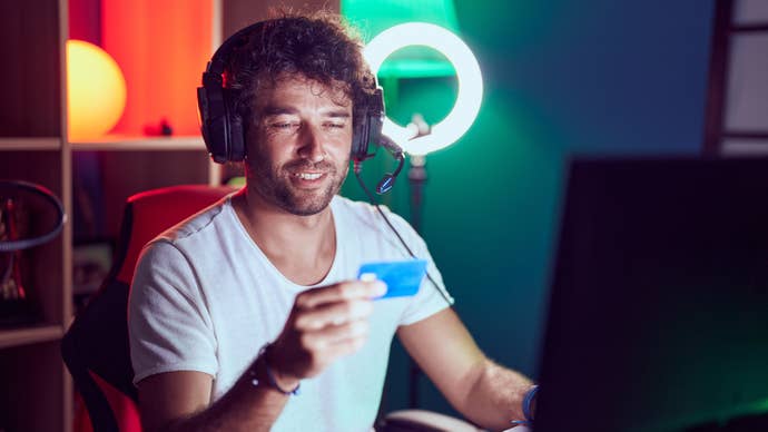 A man stares happily at his credit card, while seated playing a video game.