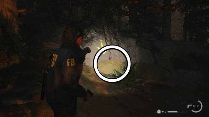 saga shining her flashlight on a key on the forest ground, below a yellow arrow painted on a stone pointing to the key