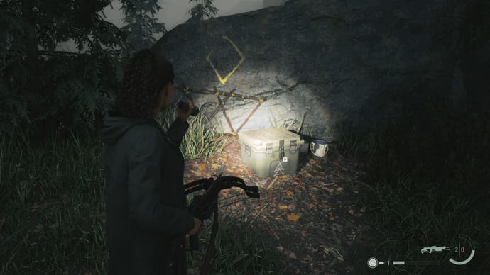 saga shining her flashlight on a cult stash by a rock wall with a yellow symbol painted on the wall above