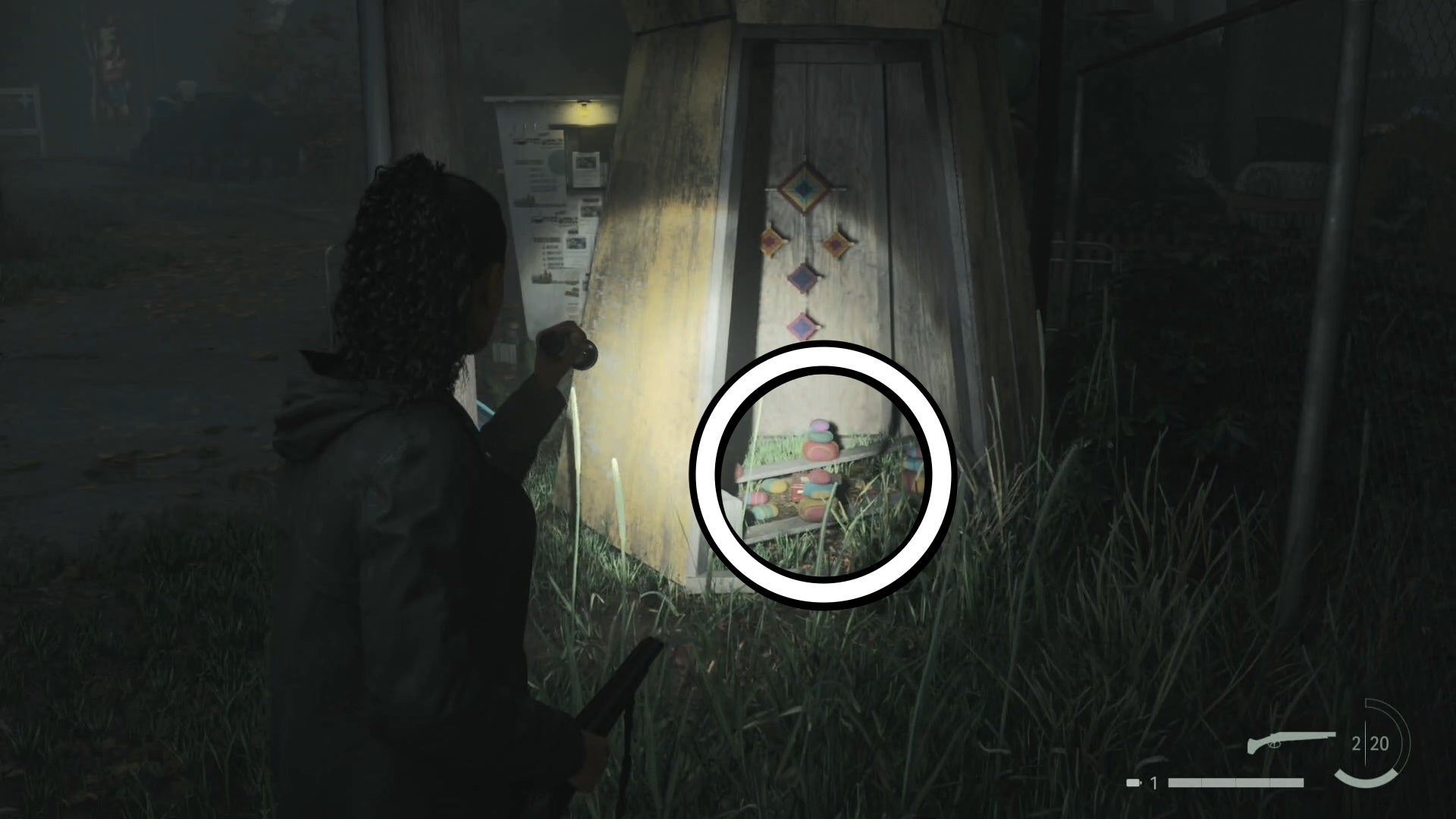 saga shining her flashlight on a lunch box inside a wooden circular structure outside a theme park in the woods