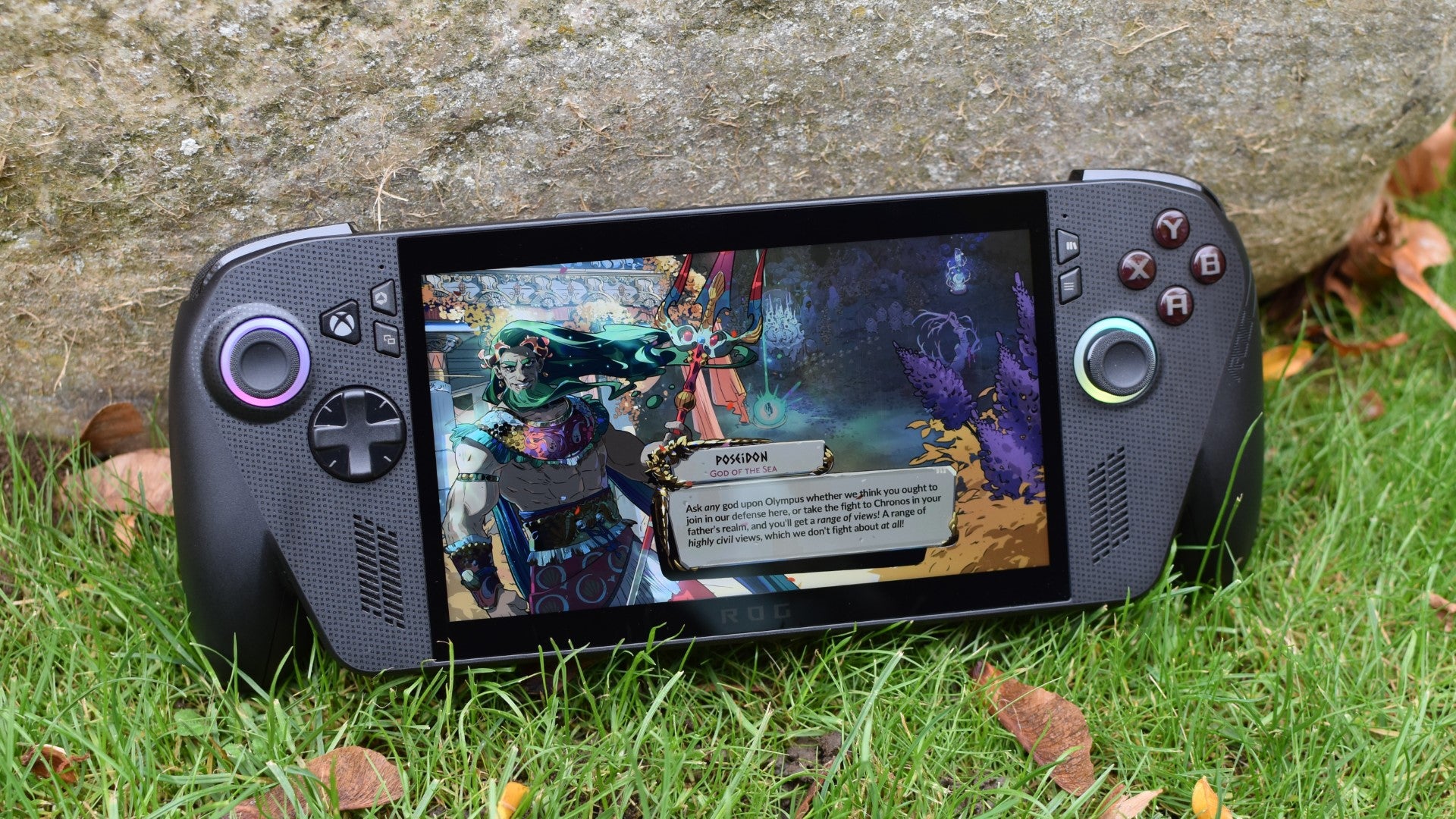 An Xbox ROG Ally X, sat on some grass, running Hades II.