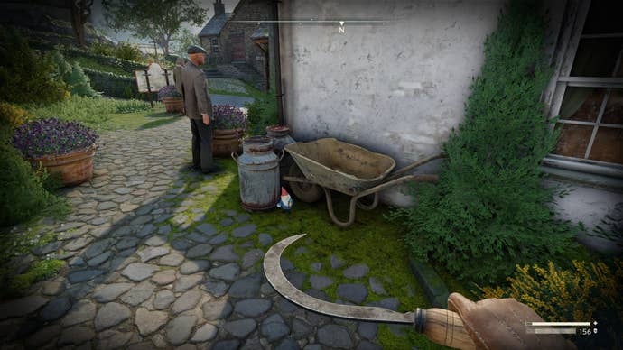 The player looks at a gnome sat beside a wheelbarrow outside of the Village Hall in Wyndham Village in Atomfall