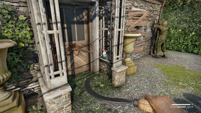 The player looks at a gnome sat inside of a house porch in Wyndham Village in Atomfall