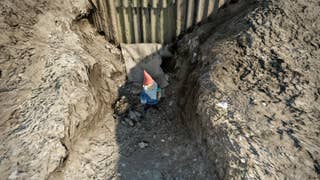 The player looks at a gnome sat in a mound of dirt in Wyndham Village in Atomfall