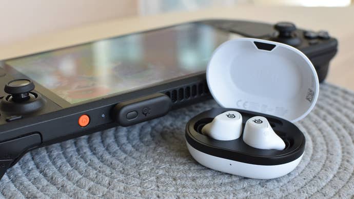 The SteelSeries Arctis Gamebuds adjacent to a Steam Deck, which has the Gamebuds' 2.4GHz receiver plugged in.