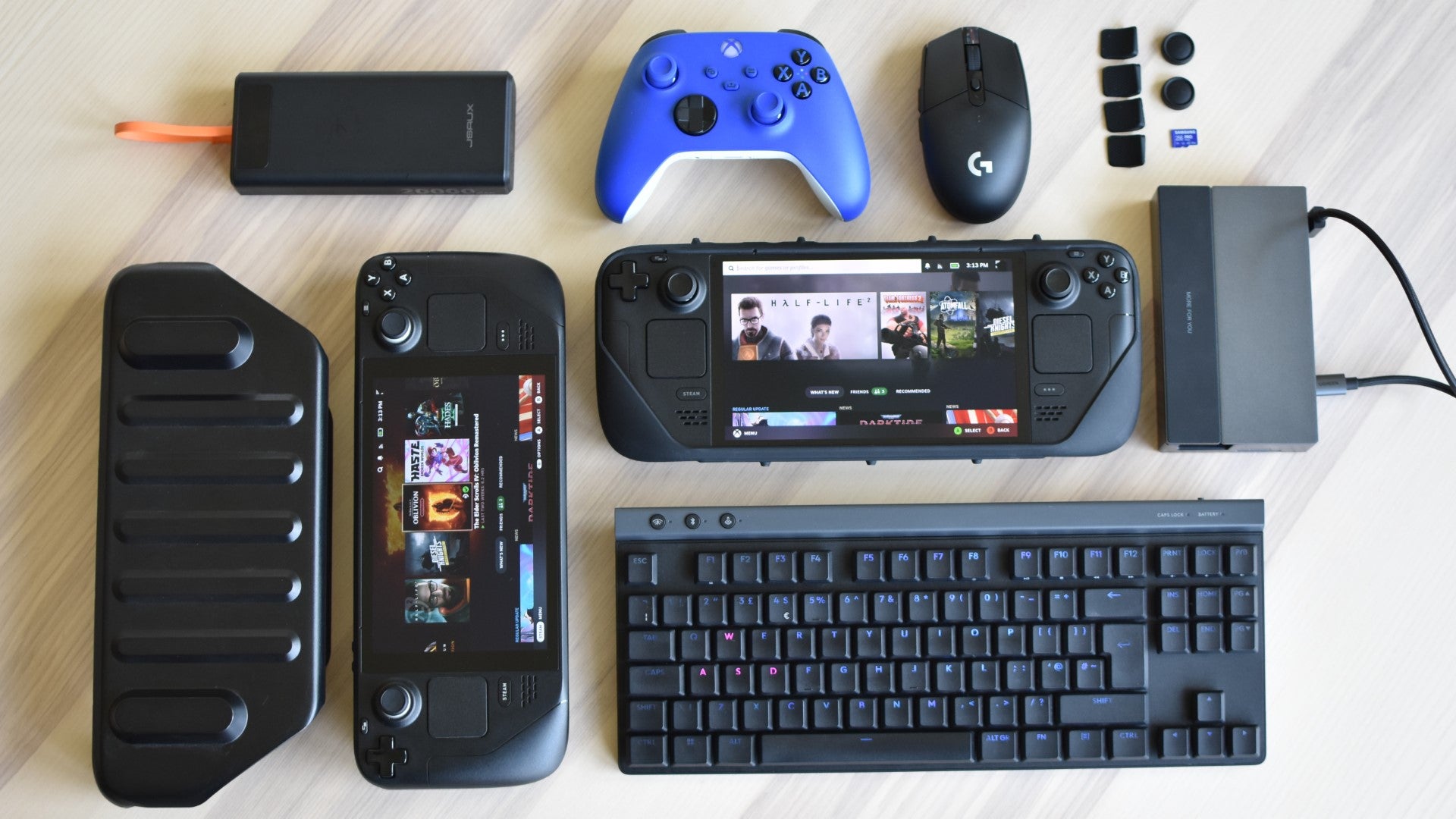 Some of the best Steam Deck accessories, and a couple of Steam Decks, laid out on a table. - 1