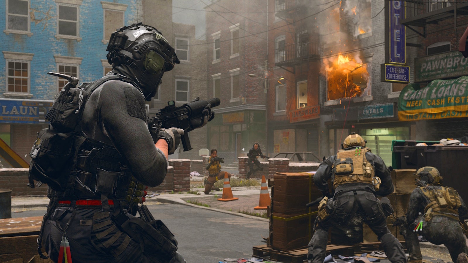 a soldier in black clothing holding a weapon and walking towards two soldiers in beige gear who are crouched behind a makeshift wall hiding from two enemy soldiers in the distance