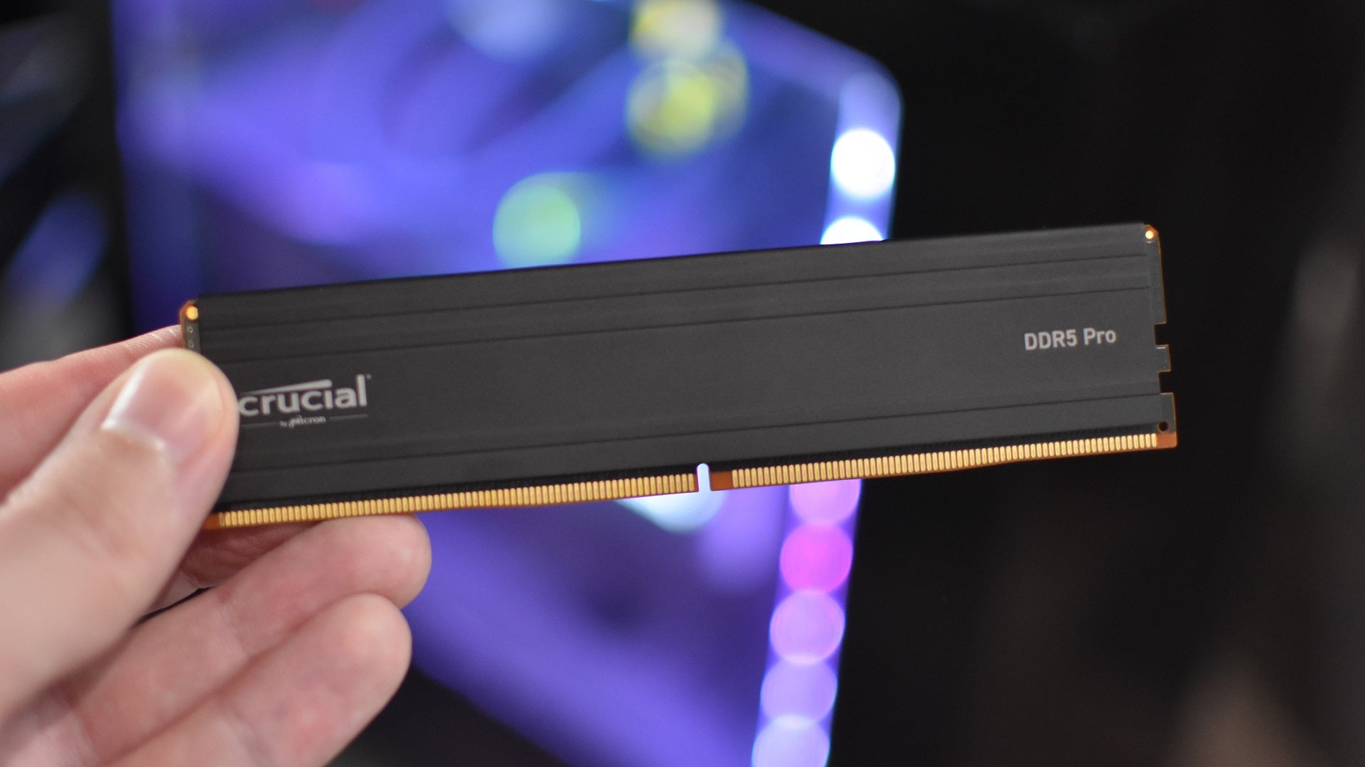 A stick of Crucial DDR5 Pro RAM being held in front of a PC. - 1