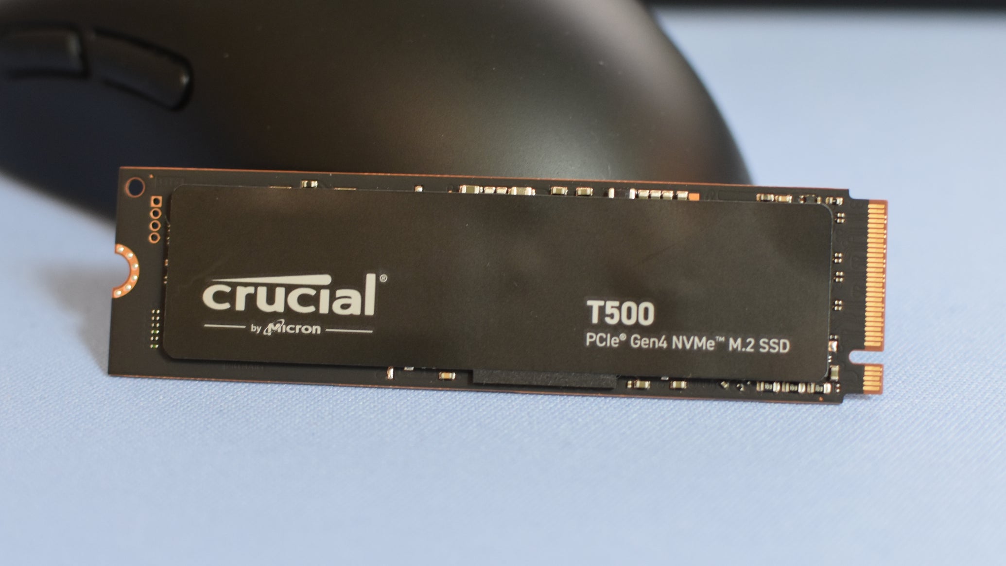 The Crucial T500 SSD propped up against a gaming mouse. - 1