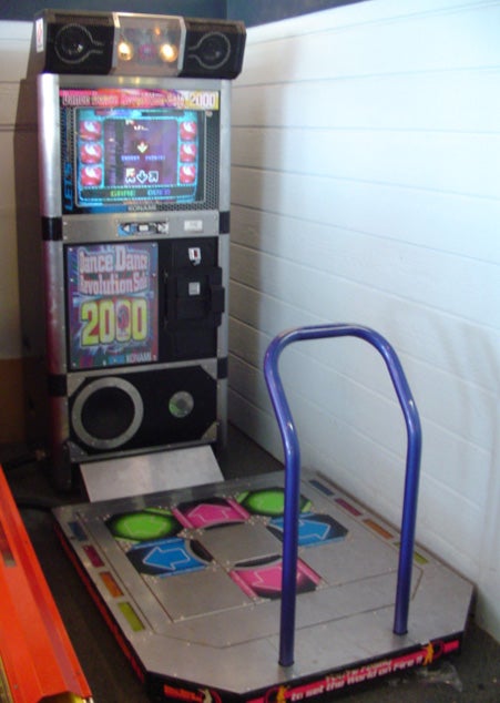 A Dance Dance Revolution arcade machine consisting of a floor pad with big coloured arrows to step on while following directions on a CRT screen.