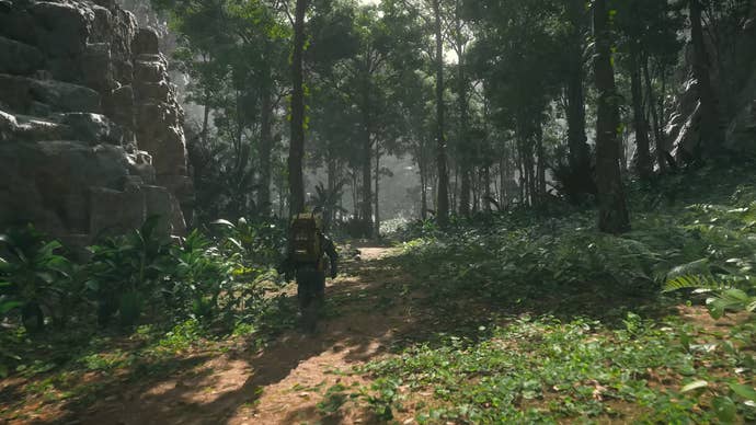 Death Stranding 2 trailer screenshot showing Sam Bridges carrying a package on his back through a lush green forest