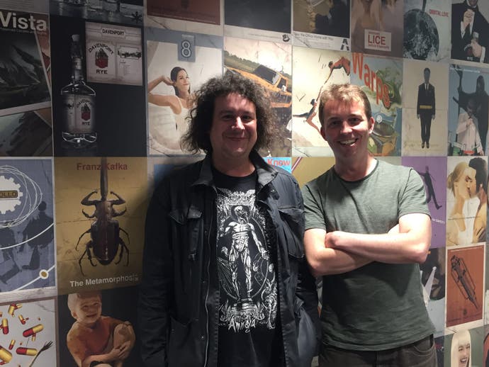 Photo of Dion Lay and Will Porter at the Creative Assembly studio in front of wall of game cover art