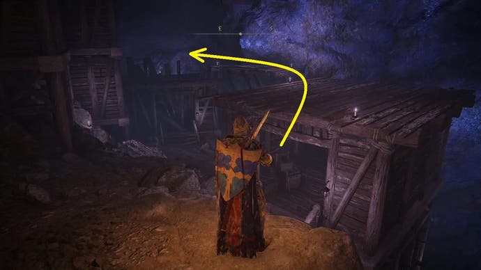 An armoured main character with a large shield on their back standing in the Sellia Crystal Tunnel in Elden Ring, with a yellow arrow pointing to the left.