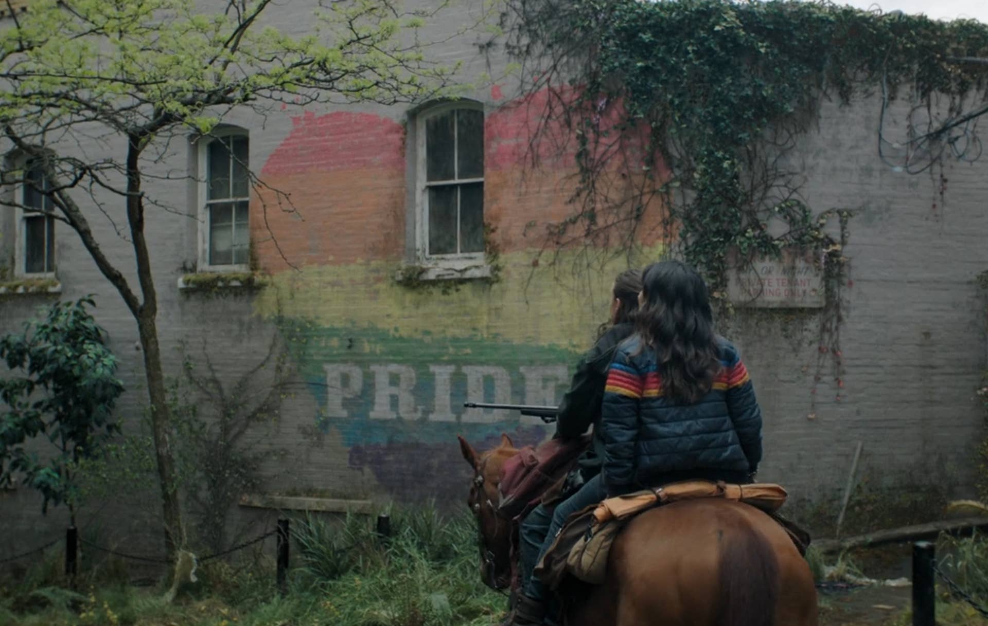 Ellie and Dina ride on the back of a horse through Seattle in TLOU season two. A rainbow heart with the word PRIDE is drawn on a nearby wall.