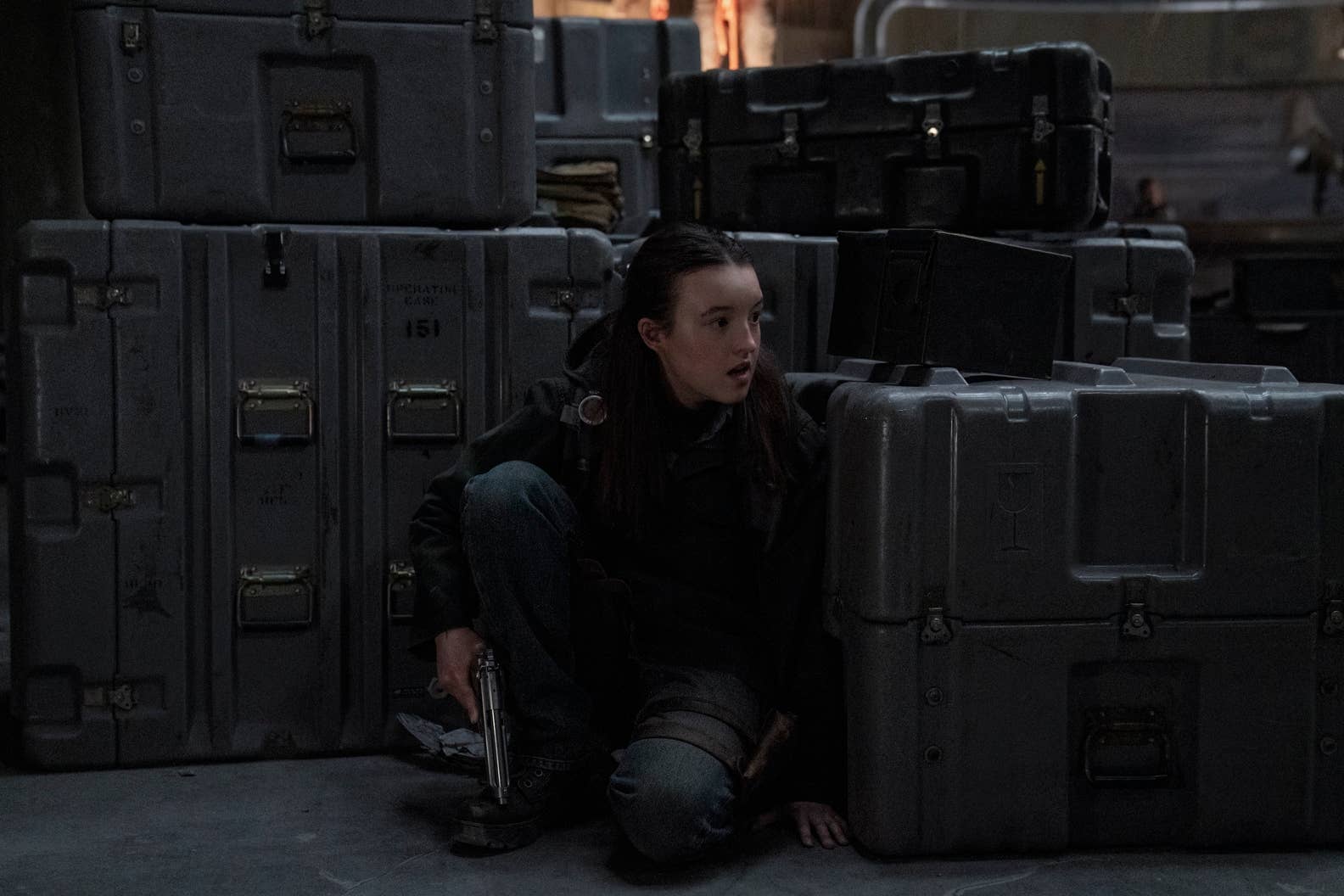 Ellie hides from the WLF behind crates in The Last of Us season two