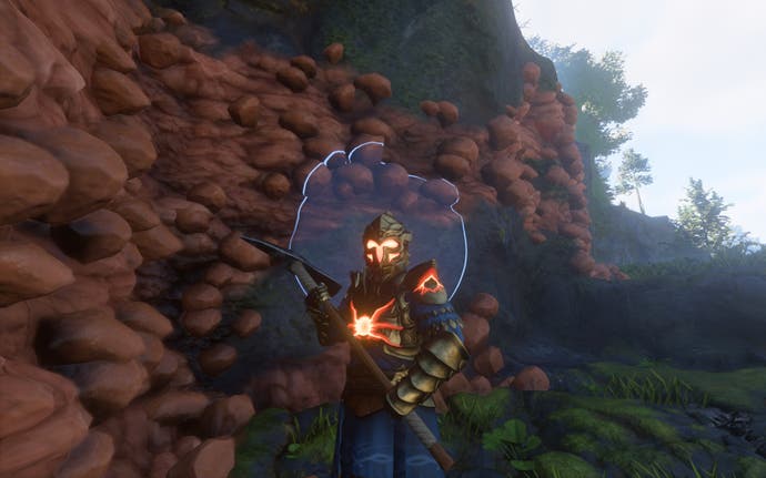 The player-character, clad in armour and holding a pickaxe, stands in front of an orange cliff filled with clay.