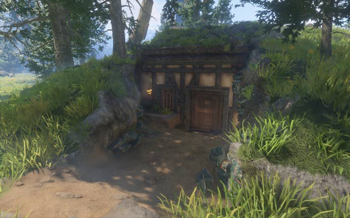 A hobbit-hole style house that has been built down into the earth, with a small window, a firefly light and a vintage wooden door.