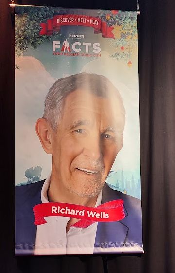 A banner at a convention showing a large picture of a white, older gentleman with cropped grey hair and an amused expression on his face.