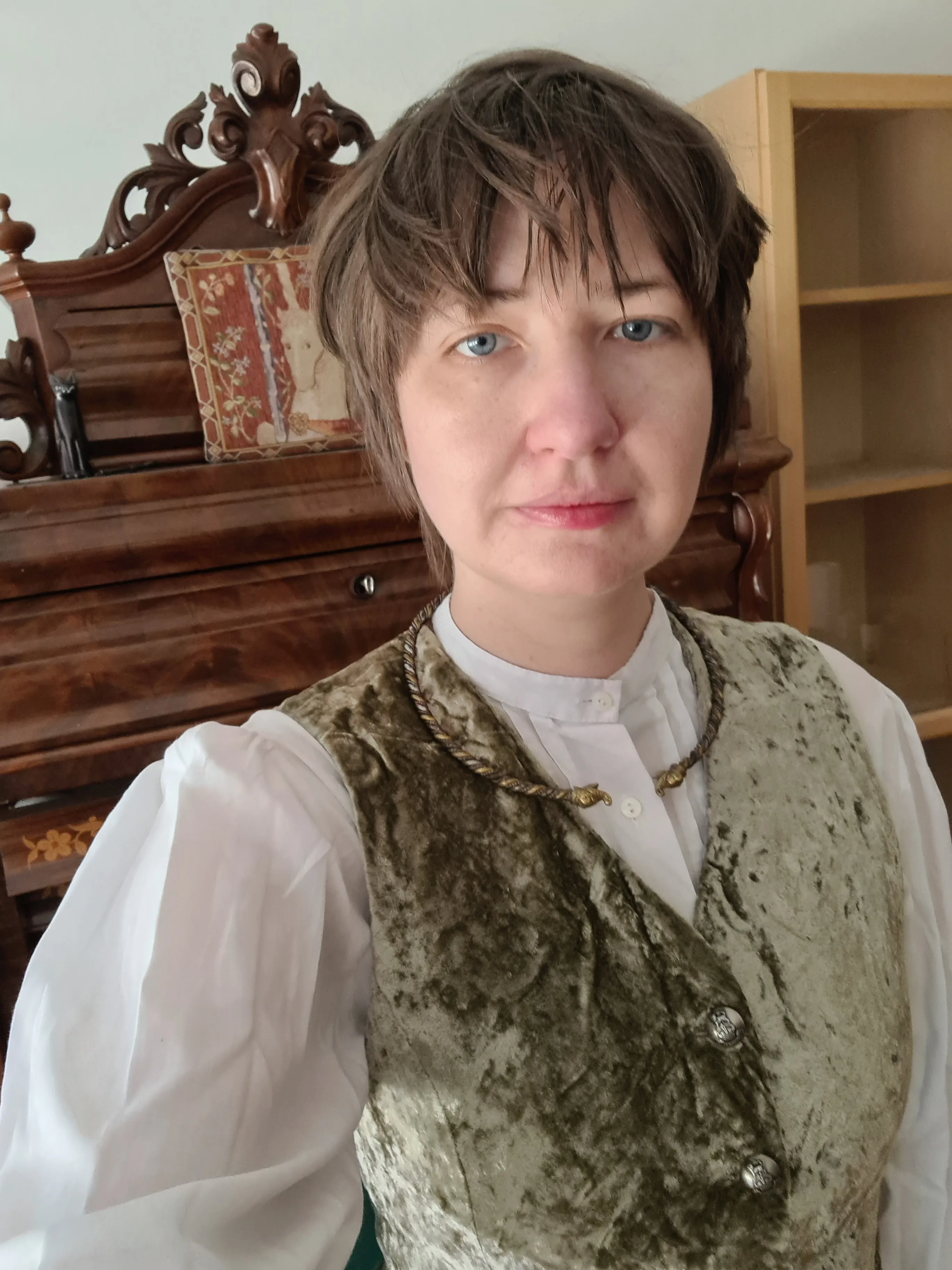 Florence Smith Nicholls, a person with short brown hair in a waistcoat and white shirt, in front of antique furniture.